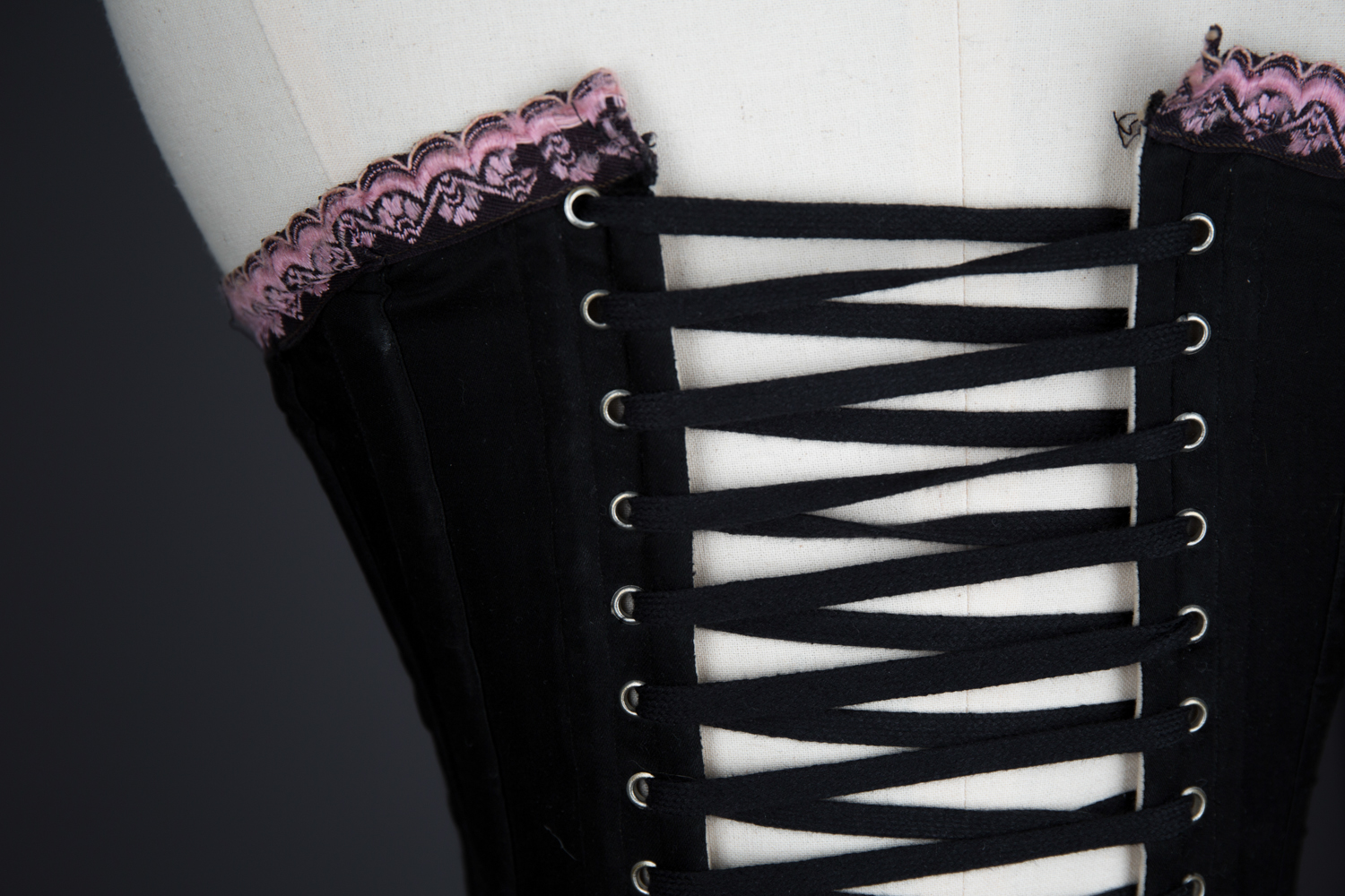 Black Cotton Corset With Spoon Busk, Pink Flossing Embroidery & Woven Trim, c. 1890-1900s, Great Britain. The Underpinnings Museum. Photography by Tigz Rice.